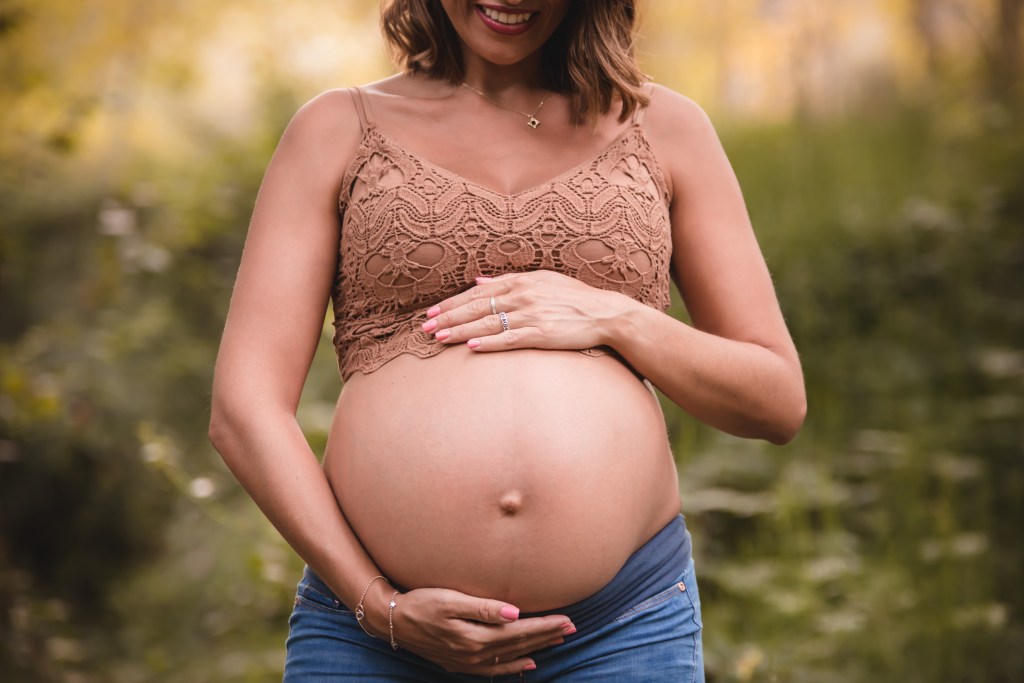 Mujer embarazada sonriendo y abrazando su barriga en un entorno natural.